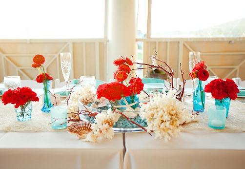 Прикрасьте столи букетами з червоних і білих квітів, пляшки з шампанським можна оформити в морському стилі